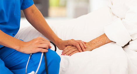 A nurse holding hands with an older patient in bed